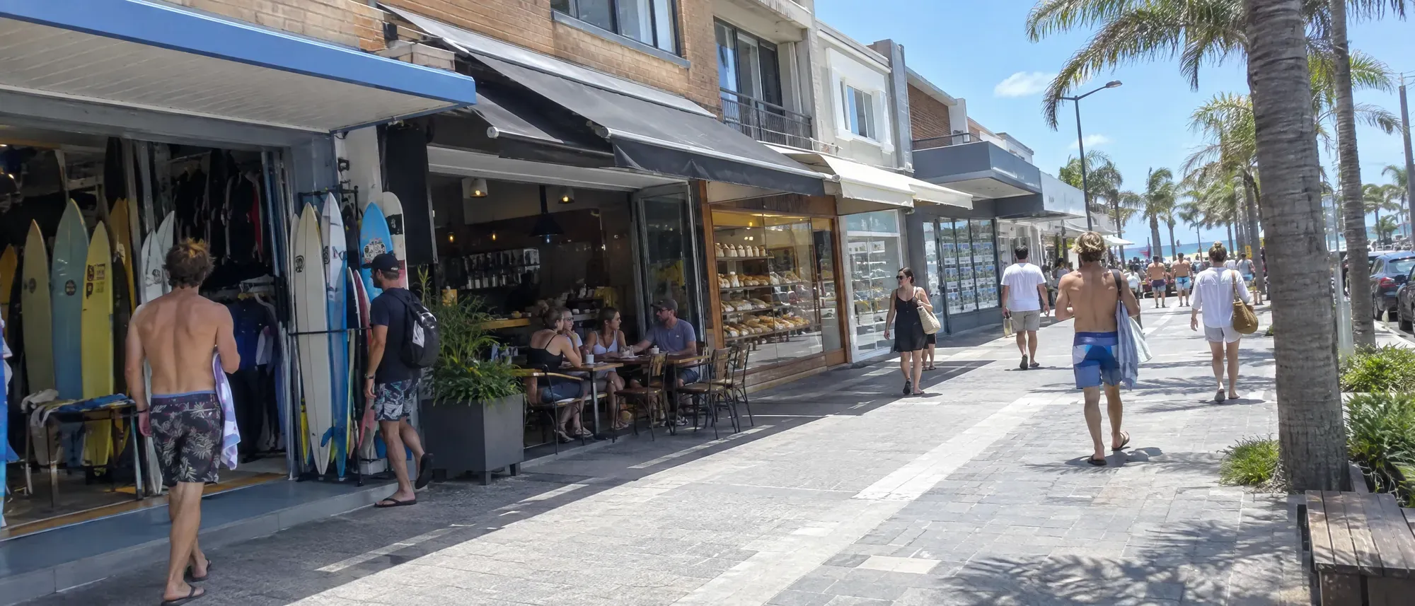 A beachside shopping street with a surf shop, cafe and bakery