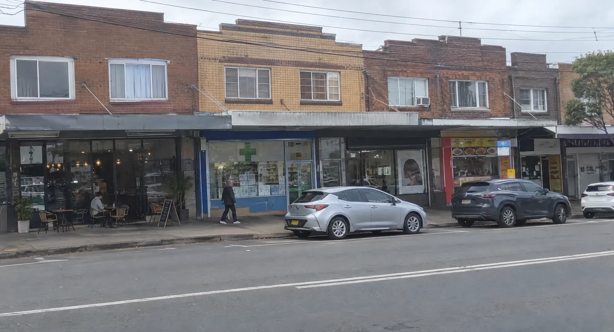 A suburban shopping strip with a cafe, pharmacy and takeaway shops